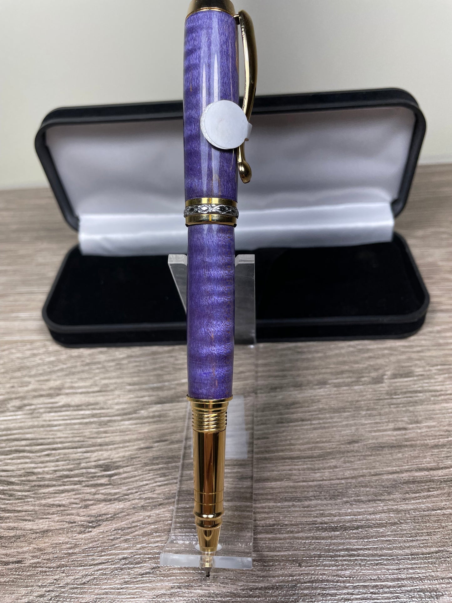 Purple pen with gold accents on a clear stand in front of an open black case.